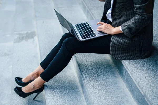 Cropped image of legs of business woman wearing heels typing on laptop. Distant work. Modern business woman. Uses gadgets