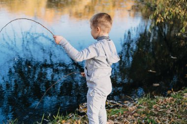 Side view of a small boy approaching the lake with a stick to play. Family, cuddle, love. Autumn, summer.
