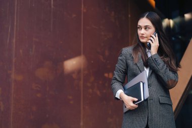 Portrait of young office assistant discussing the plan on the phone while going to a cafe during the coffee break. Copy space. Internet communication, wireless