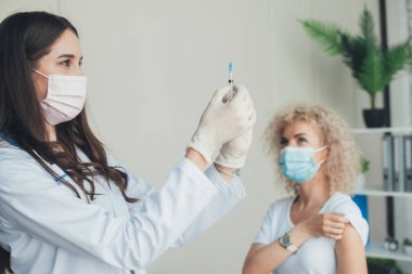 Female doctor with medical mask and gloves holding a syringe in hospital. Vaccination day. Coronavirus cure, flu medicine treatment vaccination concept.