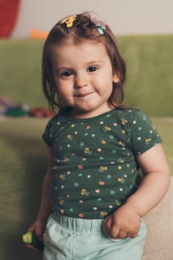 Front view of a toddler girl smiling confident having fun, standing at home looking at camera. Smiling happy child. Child care. Apartment interior. Smiling girl