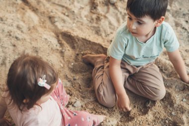 Two little kids sitting with bare feet playing on a background of sand, in the summer on vacation. Kids on playground in summer park, garden or backyard with
