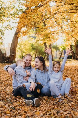 Sonbaharda ormanda dinlenirken, sarı yapraklarla kaplı zeminde poz veren güzel bir aile. - Evet. Ebeveyn, çocuk. Sağlıklı bir yaşam tarzı. Sonbahar ormanı