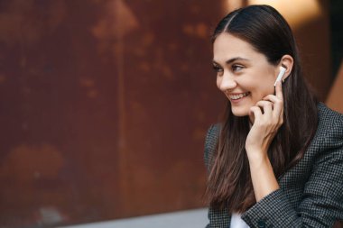 Gün batımında kablosuz kulaklık kullanan gülümseyen genç bir iş kadını cep telefonuyla video görüşmesi yapıyor. Uzayı kopyala Çevrimiçi iletişim kavramı. Uzak