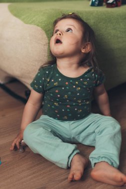 Bir yaşında, beyaz bir kız bebek yerde oturmuş yukarı bakıyor. Kız yukarı bakıyor. Yakın plan, kapalı mekan. Çocuk bakımı.