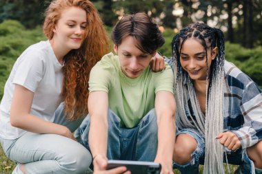 Şehir parkında cep telefonuyla video izleyen, gülümseyen bir grup genç arkadaşın yakın plan portresi. Video blogu. Arkadaşlık..