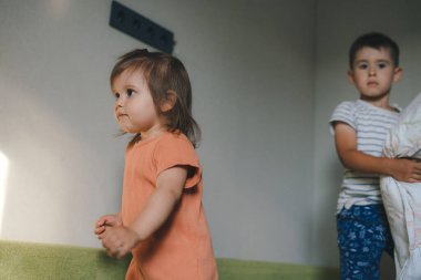 İki çocuk kanepede durmuş yastık savaşını başlatmak için doğru zamanı bekliyor, öğleden sonra evde. Mutlu aile oyunları. Mutlu aile