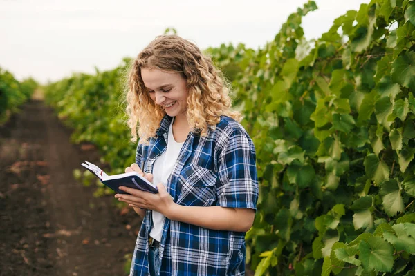 Vineyard worker checking grapes quality in vineyard and recording the observations in the notebook. Business plant agriculture concept. Business analysis