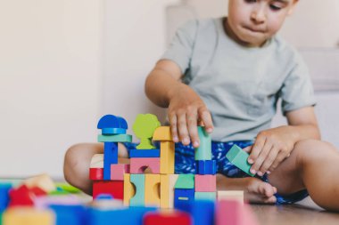 Mutlu beyaz çocuk yerde oturuyor, tuğlalardan ve bloklardan kule inşa ediyor. Oyun zamanı konsepti. Oyun odası, hafta sonları eğlenmek, aile aktiviteleri..