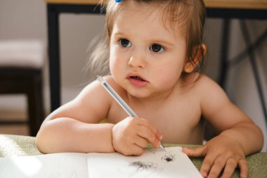 Oturma odasındaki masada oturan, ders kitabını çizen beyaz bir kızın portresi. Anaokulu oyuncakları, anaokulu. Evde ya da