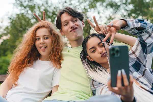 Grupa Przyjaciół Robi Sobie Selfie Smartfonem Siedzącym Ławce Parku Patrzącym — Zdjęcie stockowe
