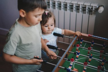 Küçük mutlu çocuklar evde masa futbolu oynuyorlar, kapalı alanda futbol oynuyorlar. Corona virüsünün kendini karantinaya alma zamanı. Mutlu bir aile. Eğlenceli aile.