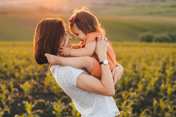 自然の上で彼女の腕の中で赤ん坊の女の子と母親の肖像画は 太陽が黄金の時間で 夜のトウモロコシ畑に設定されています 楽しい家族だ — ストック写真