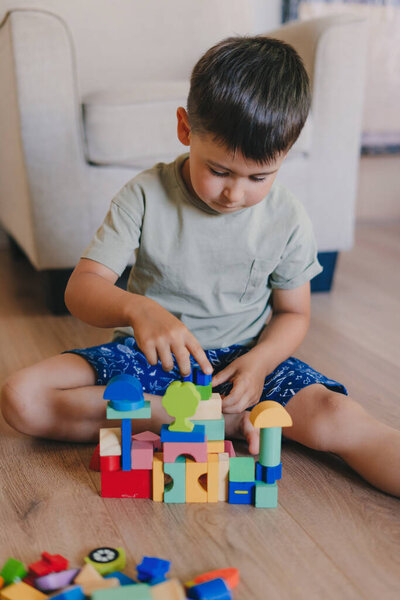Handsome caucasian little boy playing with colourful toy blocks sitting on the floor at home. Creative playing of kid development concept. Toddler kid in