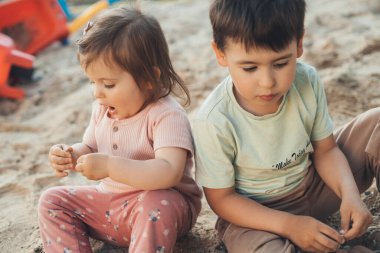 Sevimli küçük çocuk, küçük kız kardeşiyle kum çamurunda oynarken çok mutlu oldu. Çocuklar için açık hava serbest oyun kavramı. Ev bahçesi. Yaz açık hava eğlencesi