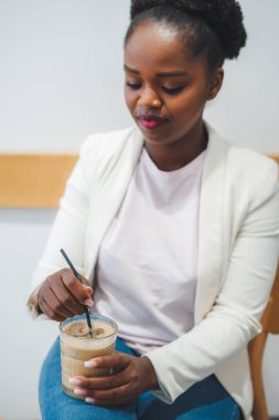 Genç, gülümseyen Afrikalı bir kadın kafeteryada oturmuş, kahve içerken dinleniyor, düşünüyor ve boş zamanların tadını çıkarıyor. Yemek molası. Güzel portre..