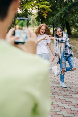 Bir çocuğun eli telefon tutarken ve parkta iki çılgın kız arkadaşının fotoğrafını çekerken yakın plan portresi. Yaz tatili eğlencesi. Cep telefonu iletişimi