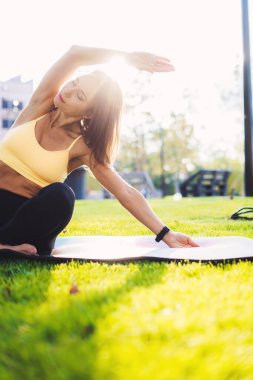 Çekici beyaz kadın yoga yapıyor, esneme egzersizleri yapıyor ve vücut parçası esnekliği için meditasyon yapıyor. Parkta antrenman, temiz hava.