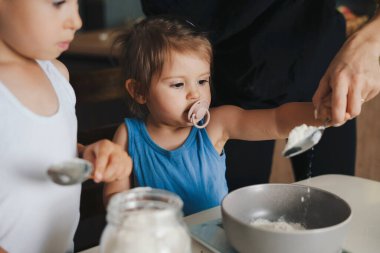 Güzel küçük kız, annemle turta pişirirken klozete un ekliyor, modern mutfakta çalışıyor. Pastanın malzemelerini ekliyorum. Mutlu aile