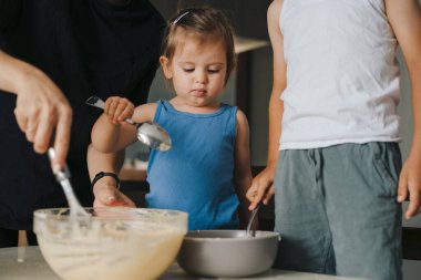 Anne, küçük sevimli çocuklara un ile sütü karıştırmayı modern mutfakta birlikte yemek yapmayı öğretiyor. Yemek pişirme süreci. Mutlu aile, çocukluk.