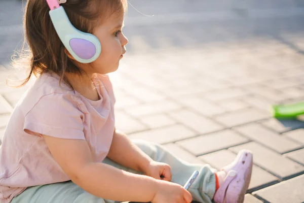 View from one side of a baby girl standing in the garden with her ears plugged to keep from catching a cold, playing and spending time developing. Child care