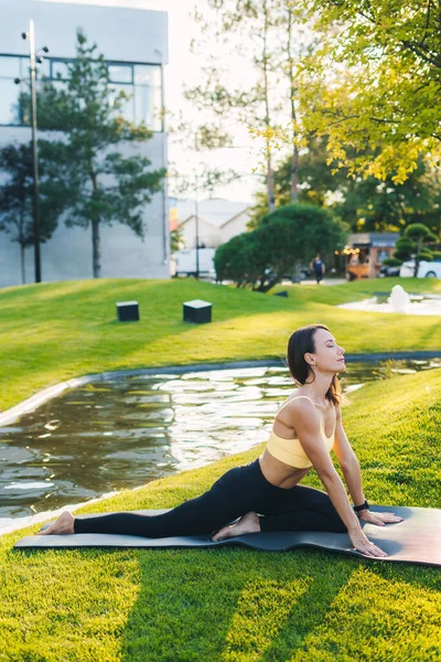 Side view of athletic woman sitting in yoga pose on fitness mat, stretching her body, on a mat in the park. Morning meditation in the park. Enjoying open-air