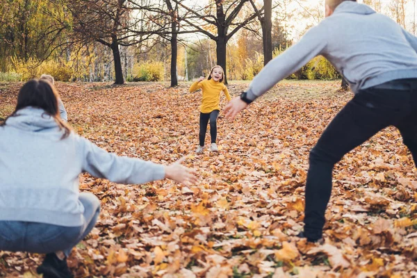 Girl running to mother and father who waiting with open arms, enjoying leisure time in autumn forest. Mother nature. Autumn forest. Happy family.