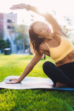 Genç bir kadın yaz sabahı parkında paspasın üzerinde egzersiz yapıyor. Yoga konsepti. Antrenman egzersizi. Sağlıklı yaşam tarzı.