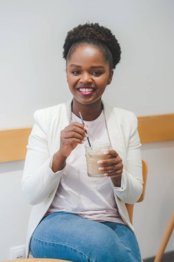 Bir bardak kahveyle gülümseyen mutlu Afro-Amerikan kadın portresi. Moda kızı, masa, tatlı içecek, lezzetli çay, aromatik kahve, smoothie