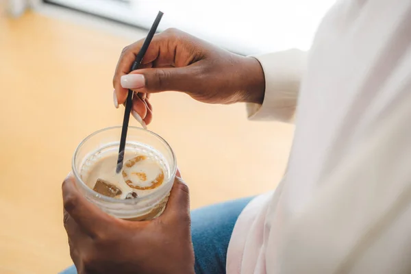 Portrait of womans hands holding a glass of iced-coffee in a street cafe. Lady is enjoying a cold drink alone. Businesswoman enjoys relaxing with glass of