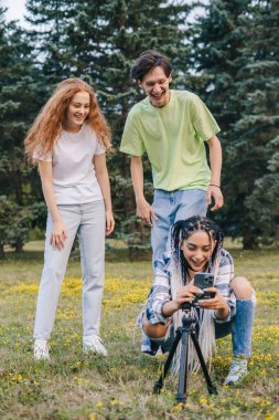 Genç üç nüfuzlu kişi, takipçileri için selfie çekmek için telefon tripodunu tamir ediyor. İnternette popülerlik, arkadaşlık. Sosyal medya için içerik oluşturuluyor