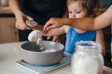 Anne ve çocukları doğum günü pastası malzemelerini tartıp eğleniyorlar. Aile değerleri, tecrübe yoluyla öğrenme. Eğlenceli aile..
