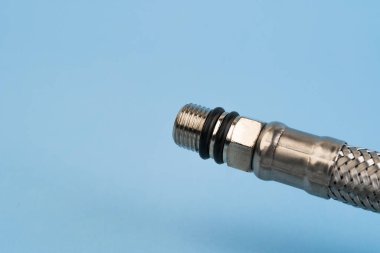 Mavi arka planda bulunan musluğa esnek bağlı güçlendirilmiş metal hortum..