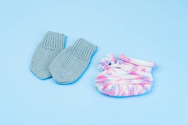 El yapımı pembe ve beyaz çizme ve mavi arka planda izole edilmiş prematüre bebekler için yün eldivenler.