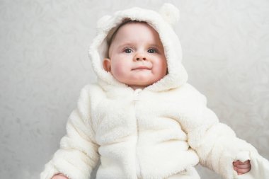 Beyaz kürklü tatlı bir kız bebek, arka planda gülümsüyor..
