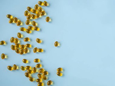 Mavi bir yüzeyde vitamin kapsülleri. D vitamini. Omega-3. Sağlık hizmetleri. Besleyici takviyeler. Sağlıklı beslenme. Mutluluk hapları. İyimser haplar. Zihinsel ve fiziksel sağlık. Düz yatıyordu