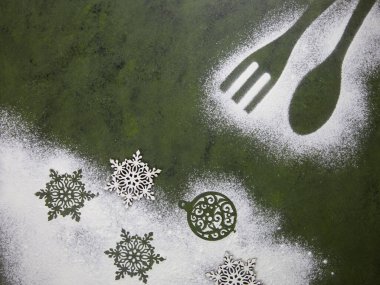 Un kar taneleri ve mutfak aksesuarlarıyla Noel ağacı yeşili arka plan. Noel tatili kurabiyeleri. Mutfak masasında un desenleri var..