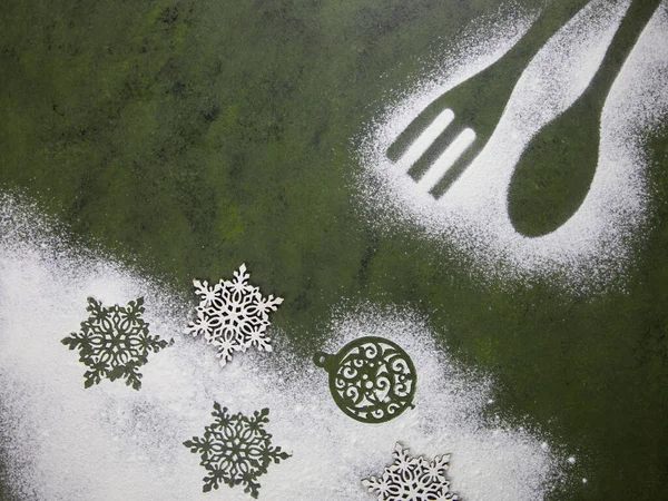 Un kar taneleri ve mutfak aksesuarlarıyla Noel ağacı yeşili arka plan. Noel tatili kurabiyeleri. Mutfak masasında un desenleri var..