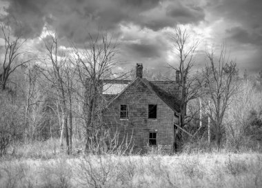 Baharda Kanada 'nın kırsal kesimindeki bir çiftlik bahçesinde terk edilmiş, eski, siyah beyaz, ürkütücü görünümlü bir ev.