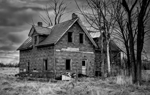 Baharda Kanada 'nın kırsal kesimindeki bir çiftlik bahçesinde terk edilmiş, eski, siyah beyaz, ürkütücü görünümlü bir ev.