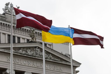 RIGA, LATVIA. 17 Şubat 2022. Seçici odak fotoğrafı. Letonya ve Ukrayna bayrakları Letonya Ulusal Operası önünde dalgalanıyor.