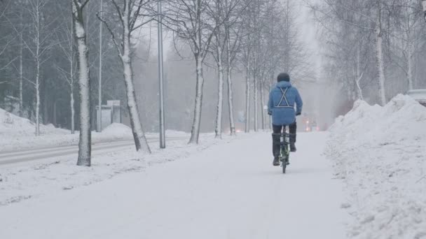 A kerékpáros mozog az utcán a hóvihar alatt. — Stock videók