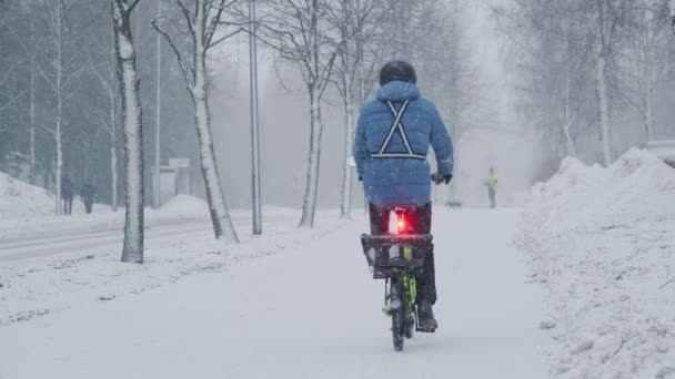 Ο ποδηλάτης κινείται στο δρόμο κατά τη διάρκεια της χιονοθύελλας. — Αρχείο Βίντεο