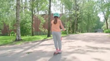 The girl in the blue helmet rides a scooter along a European city street on a summer sunny day