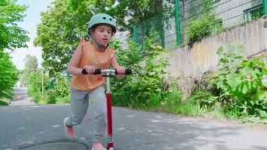 The girl in the blue helmet rides a scooter along a European city street on a summer sunny day. Slow-motion footage