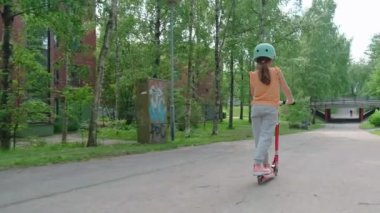 The girl in the blue helmet rides a scooter along a European city street on a summer sunny day
