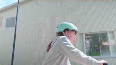 The girl in the blue helmet rides a scooter along a European city street on a summer sunny day. Slow-motion footage