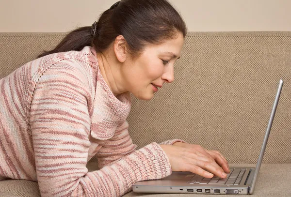 Seniorkvinne med bærbar pc, avslappende på sofaen . – stockfoto