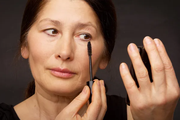 Frau mit nackten Schultern sieht Spiegel malt Wimpern — Stockfoto