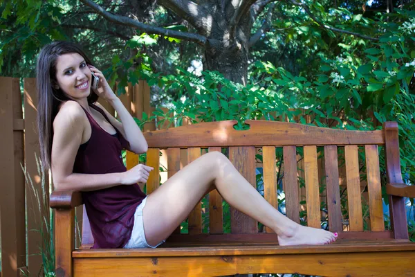 Pretty teen girl talking on phone on a bench outside - copyspace — Stock Photo, Image